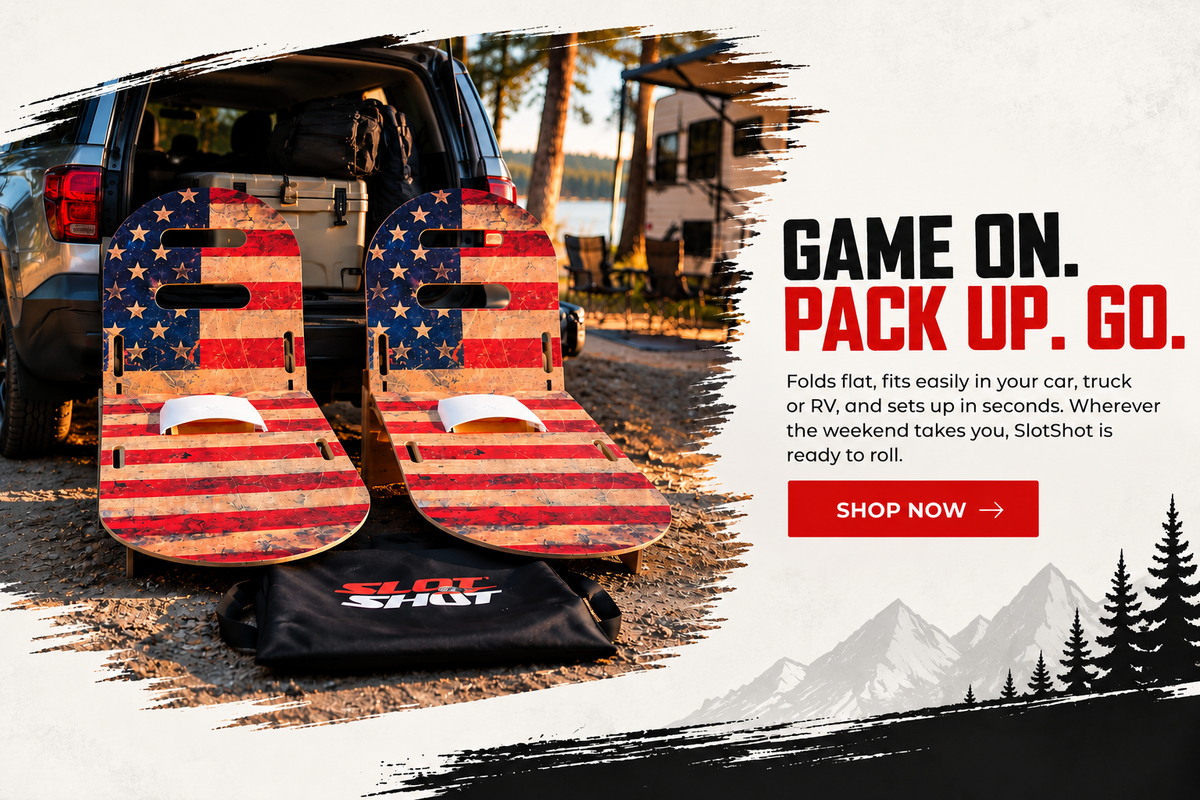Two red, white, and blue American flag patterned SlotShots are displayed in the back of a black SUV with a black SlotShot bag underneath them, set against a rustic outdoor campsite background. The image features a white graphic overlay on the right with text reading 'GAME ON.