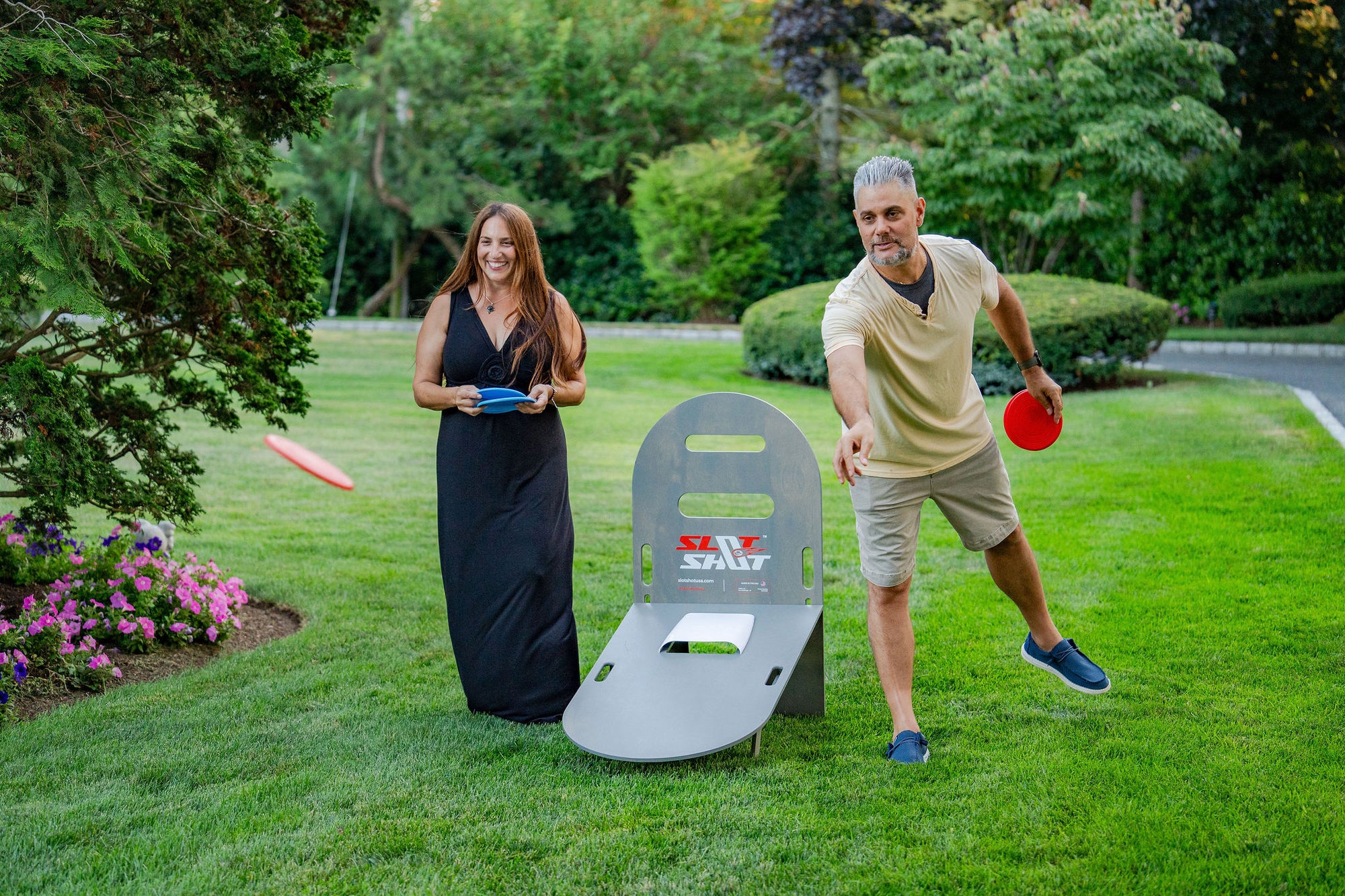 Couple playing SlotShot backyard disc game on the lawn with oyster board and red and blue discs