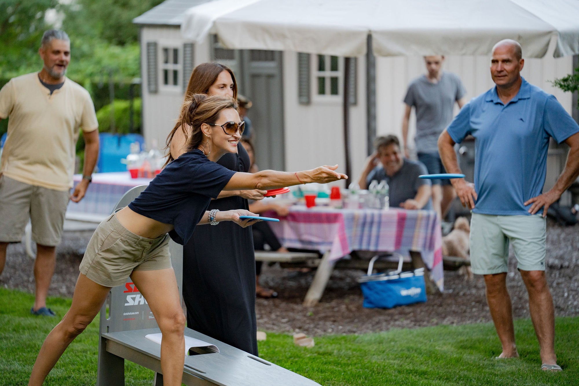 Friends playing SlotShot backyard disc game at a summer party with tables and drinks in the background