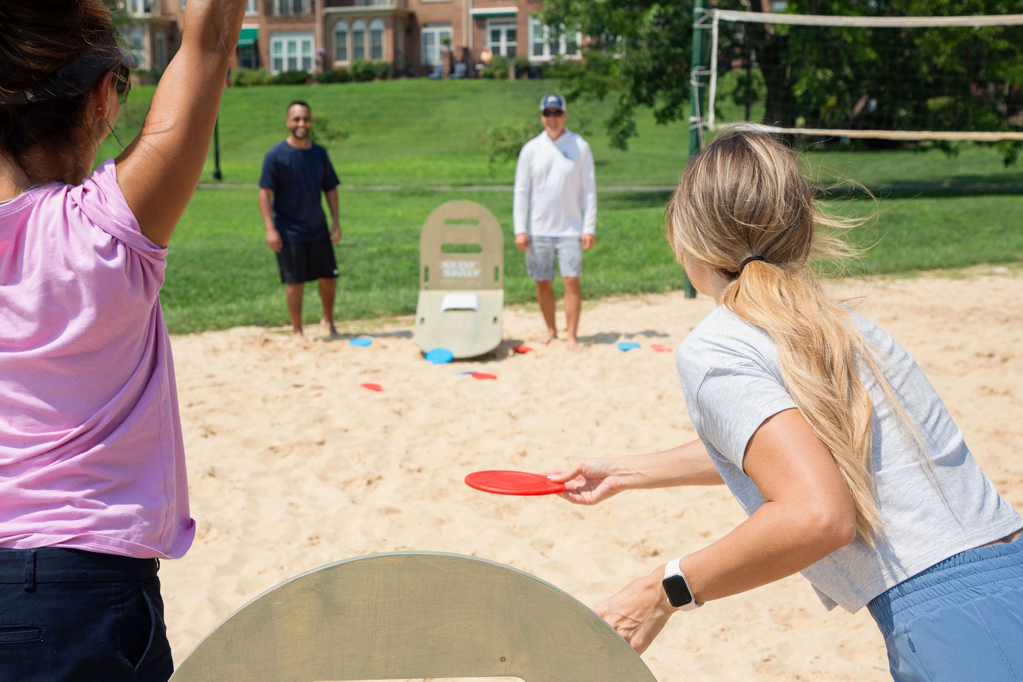Friends playing SlotShot backyard game on a sandy court near a volleyball net