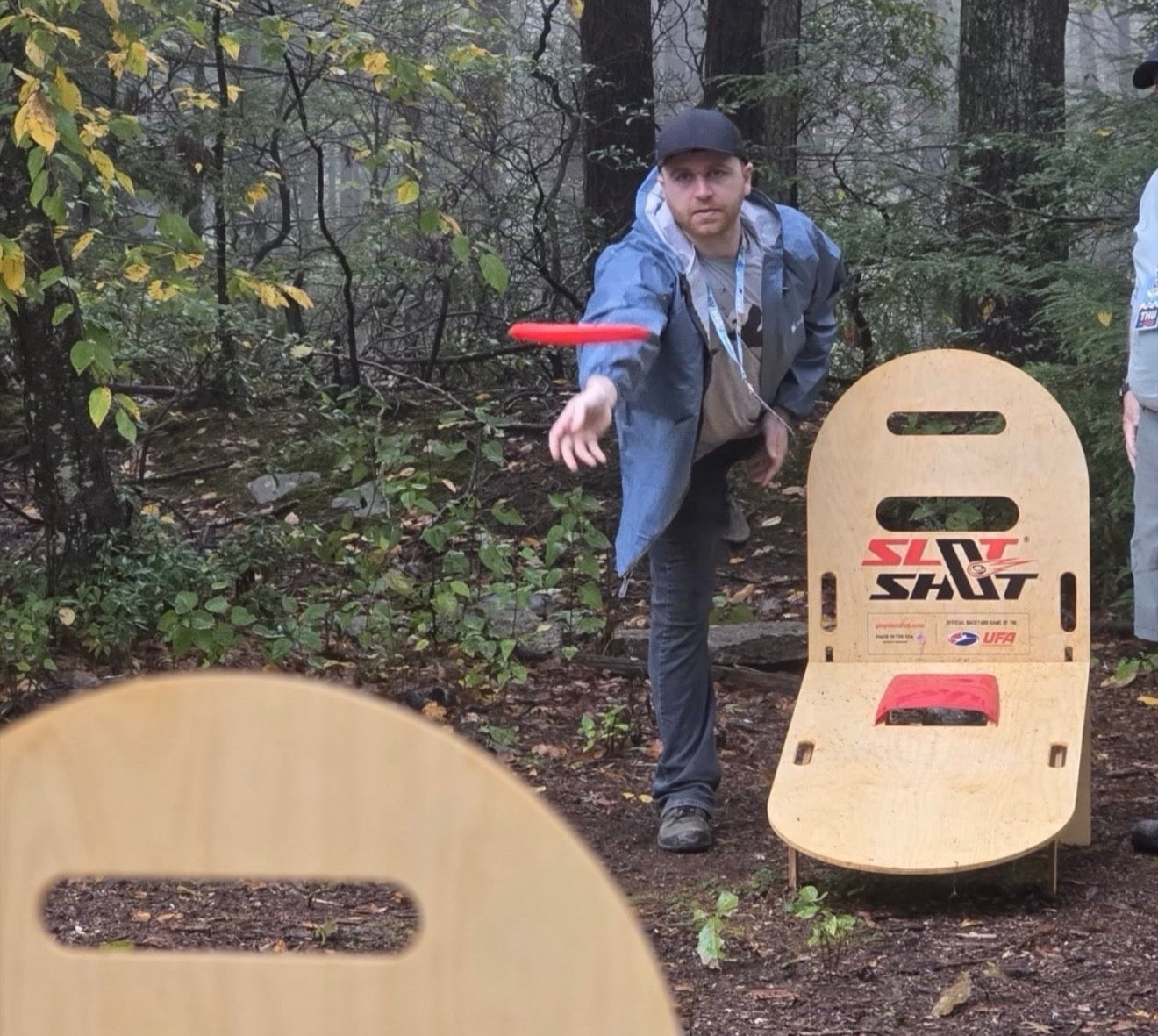 Person throwing a red disc while playing SlotShot backyard game in the woods at DGPT MVP Open Event