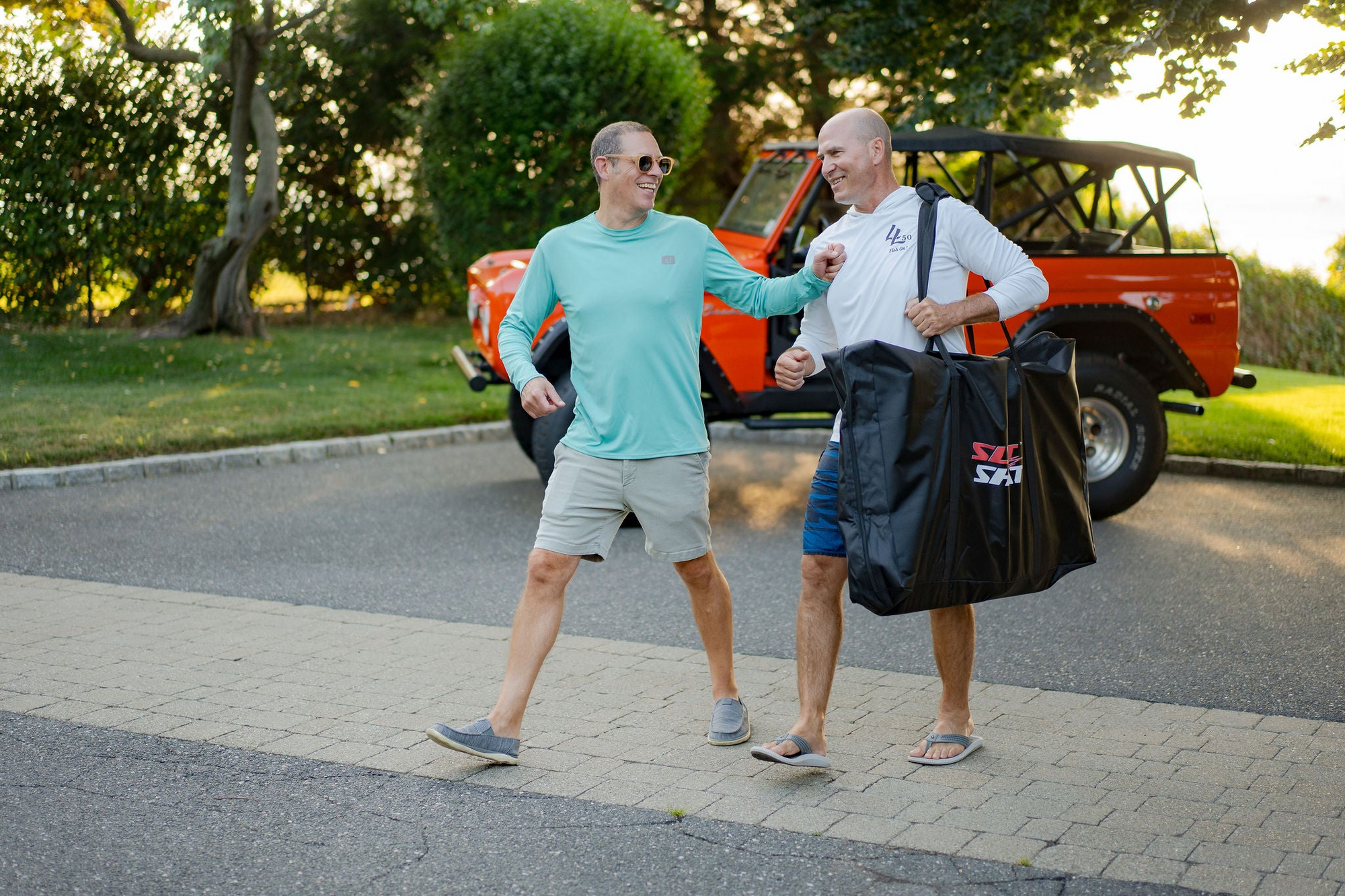 Two friends walking with a SlotShot game carry bag and smiling near an orange ford bronco after outdoor play